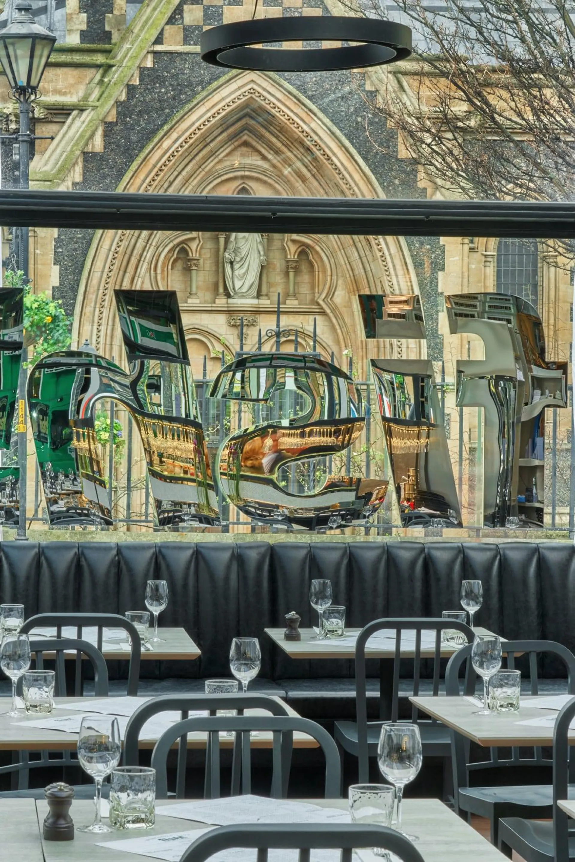 Outdoor restaurant terrace with black chairs and tables set for dining, overlooking a historic Gothic church facade with ornate stone archway and statue.