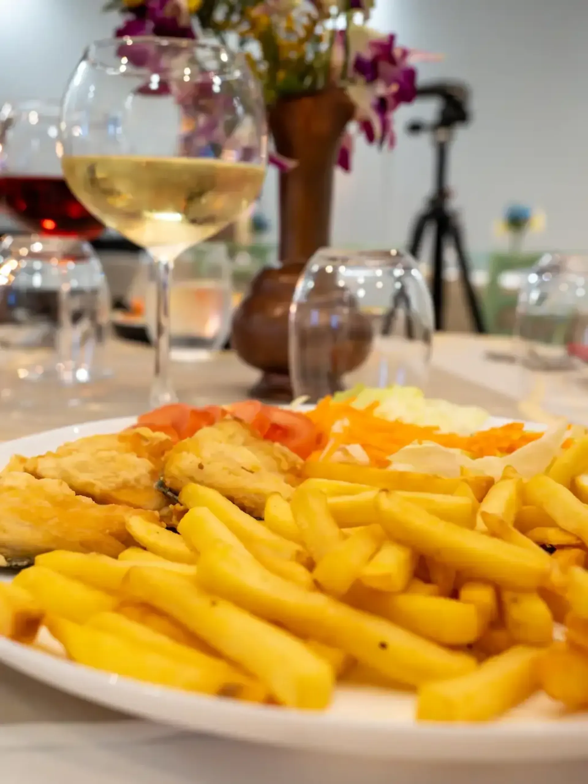 Fried fish fillets served with french fries and salad at the restaurant, with a glass of white wine and a decorated table in the background