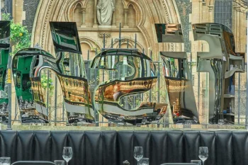 Outdoor restaurant terrace with black chairs and tables set for dining, overlooking a historic Gothic church facade with ornate stone archway and statue.