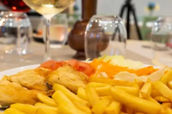 Fried fish fillets served with french fries and salad at the restaurant, with a glass of white wine and a decorated table in the background