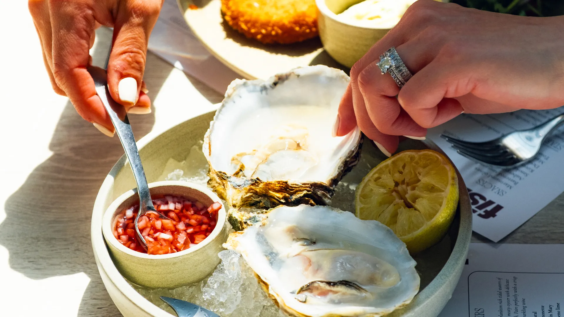 Person eating fresh oysters with cocktail sauce and lemon at an outdoor seafood meal on a sunny day