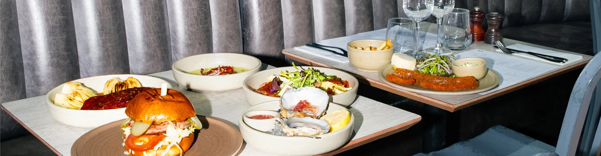 Fine dining table setting with gourmet dishes including seafood, burger, and salads, accompanied by glassware and table linens in an upscale restaurant