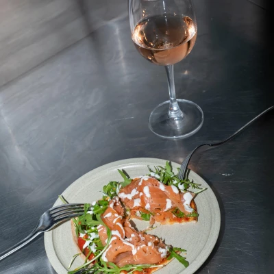 Elegant plated dish with smoked salmon, microgreens, and white cream sauce on a grey plate, accompanied by a glass of rosé wine and fork on dark surface.
